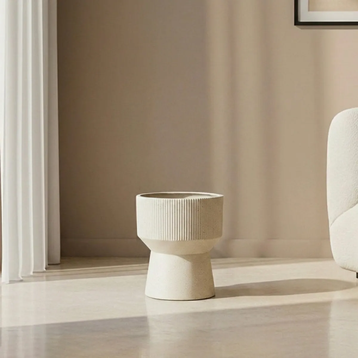 Off-white hourglass planter shown empty on a sunlit living room floor.
