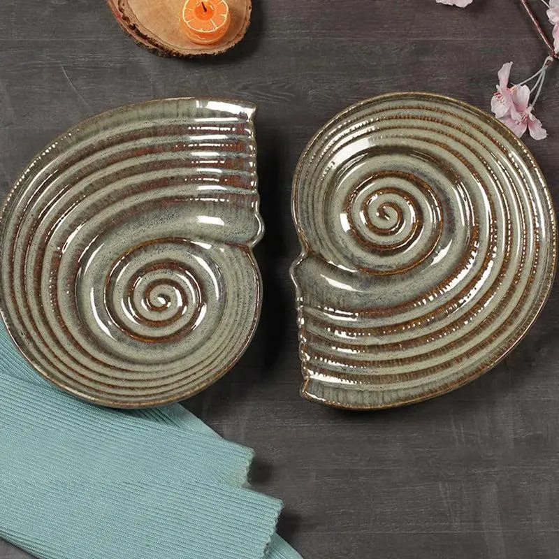 Two glossy green and brown spiral ceramic platters arranged on a dark surface