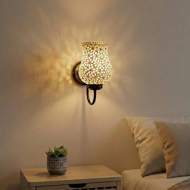 White mosaic glass wall lamp glowing on a beige wall beside a bedside table