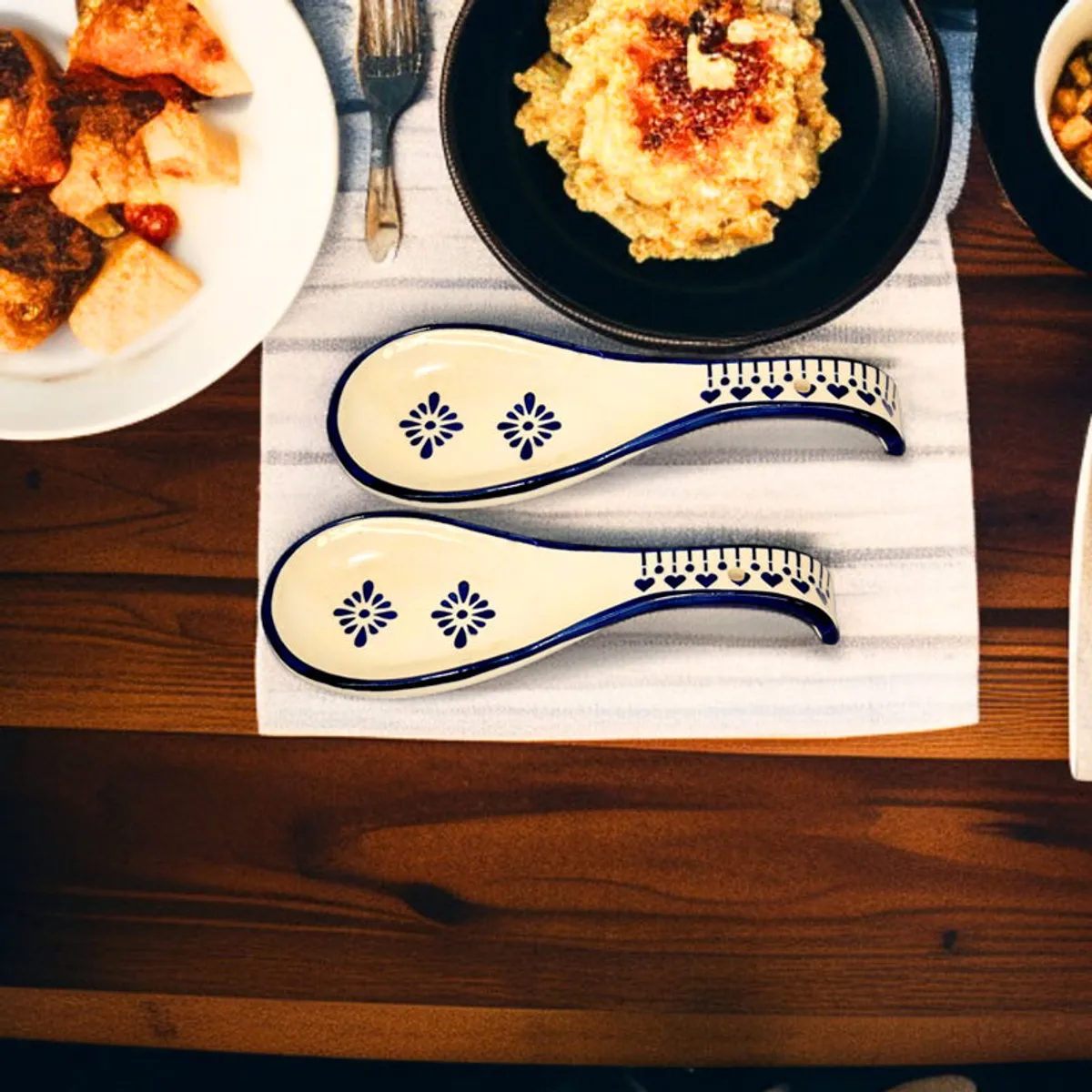 Two blue and white ceramic spoon rests arranged on a striped table runner