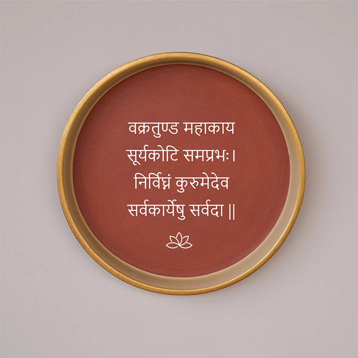 Close-up of a round brown wall plate with white Sanskrit script and lotus motif