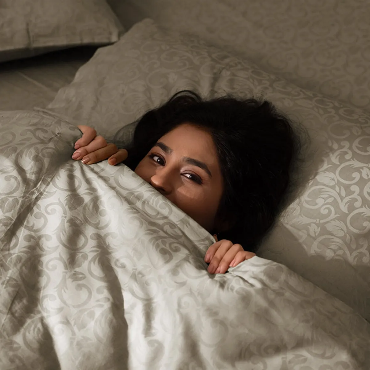 Person relaxing under a beige floral patterned bedsheet