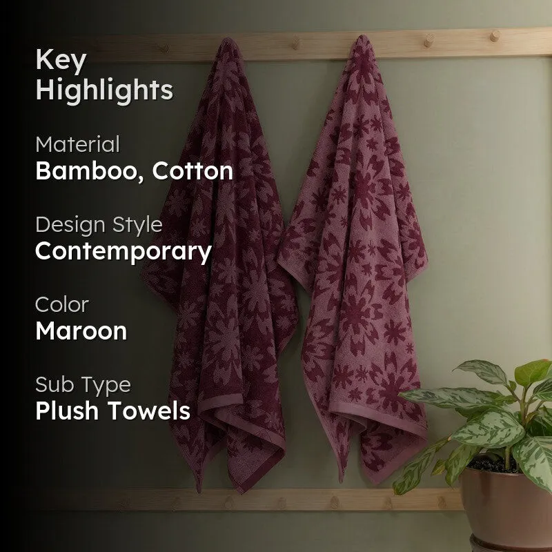 Maroon floral bath towels hanging on a wooden rack in a bathroom setting.
