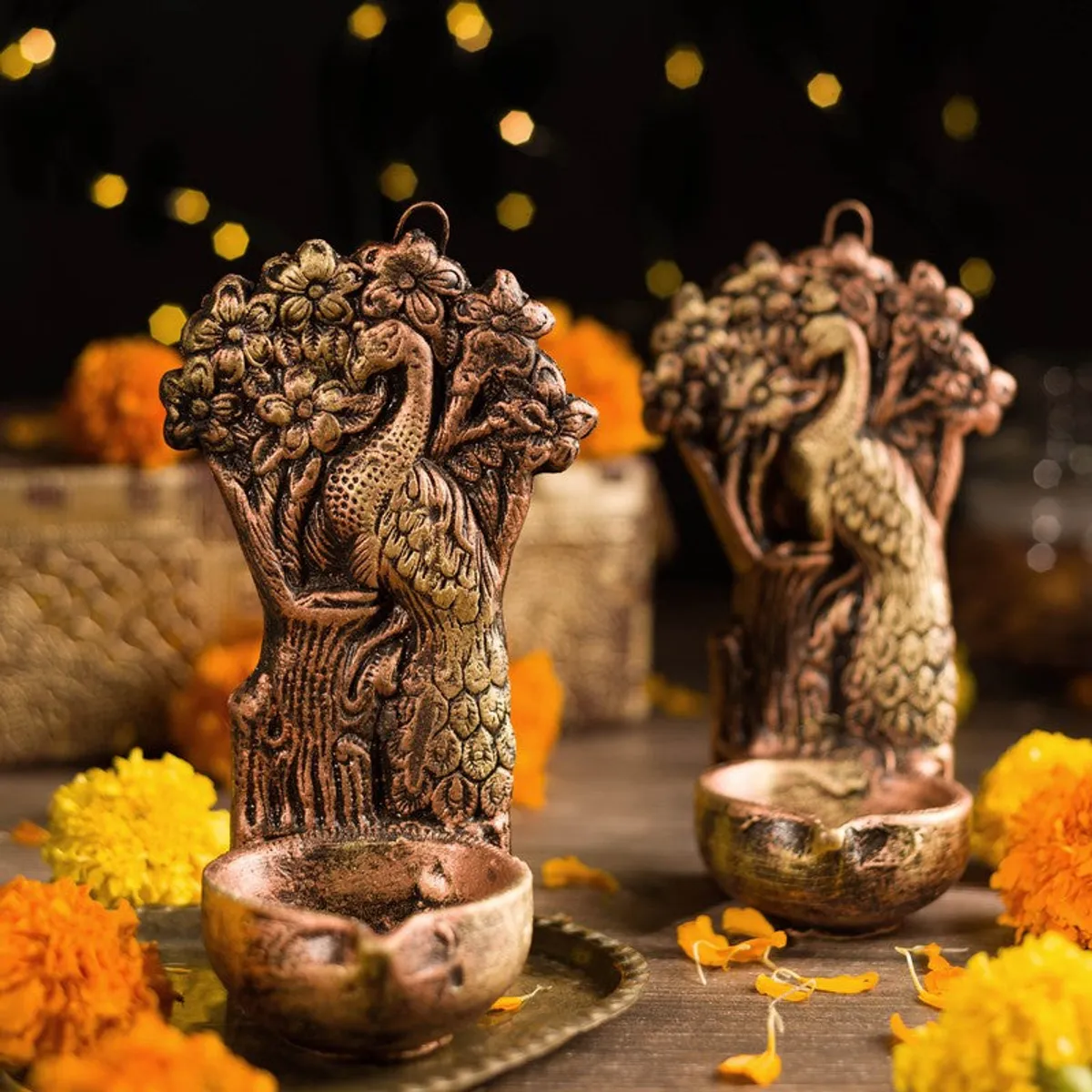 Close view of a peacock diya pair with warm candlelight and marigold flowers