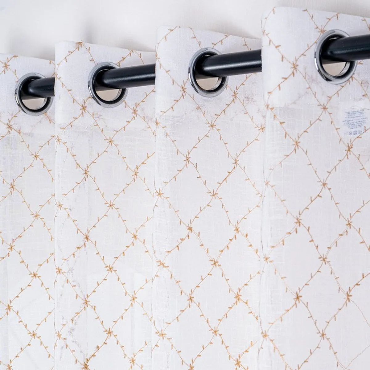Close view of silver eyelets on a white curtain with gold embroidery.
