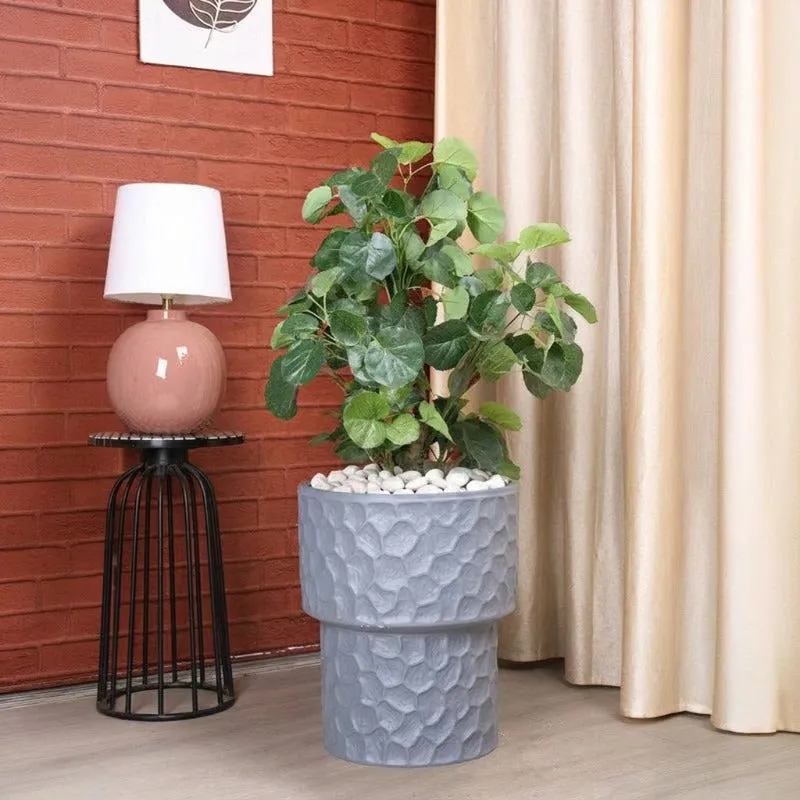 Grey textured planter with a leafy plant beside a lamp and curtains