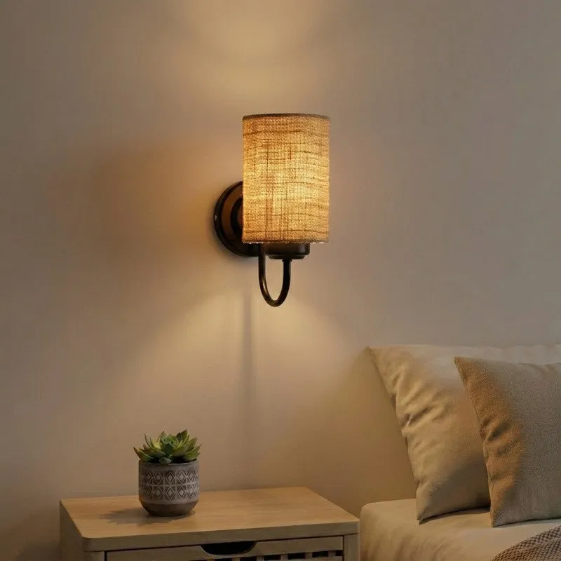 Brown jute wall lamp with black iron base mounted beside a bed