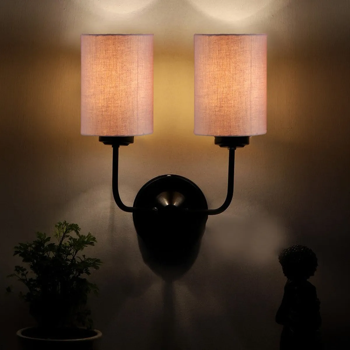 Lit beige wall lamp with black iron mount against a dark wall