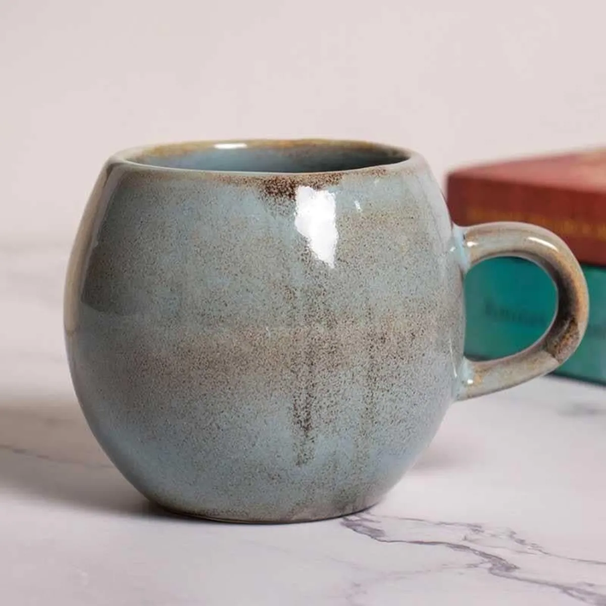 Grey speckled mug with rounded shape and handle displayed beside a maroon box