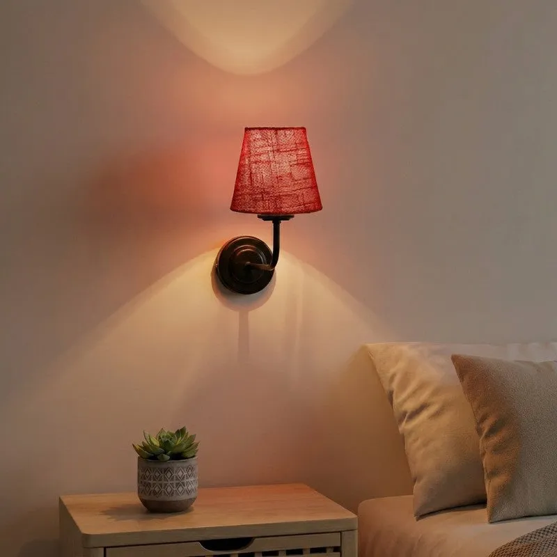 Red jute wall lamp with black iron arm mounted beside a bed