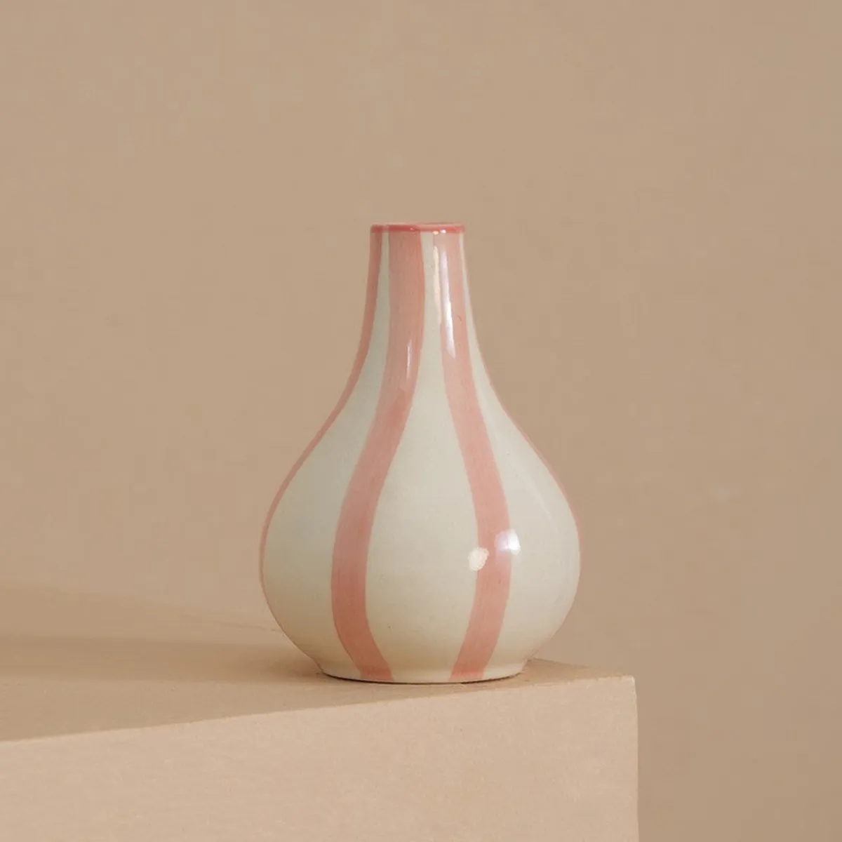 White and pink striped ceramic vase on a beige plinth