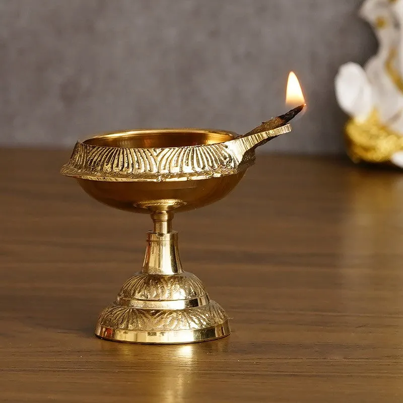 Close view of a gold brass diya with a lit wick on a dark wooden surface.