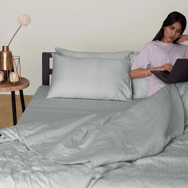 Light grey patterned duvet cover and pillow on a bed beside a seated woman