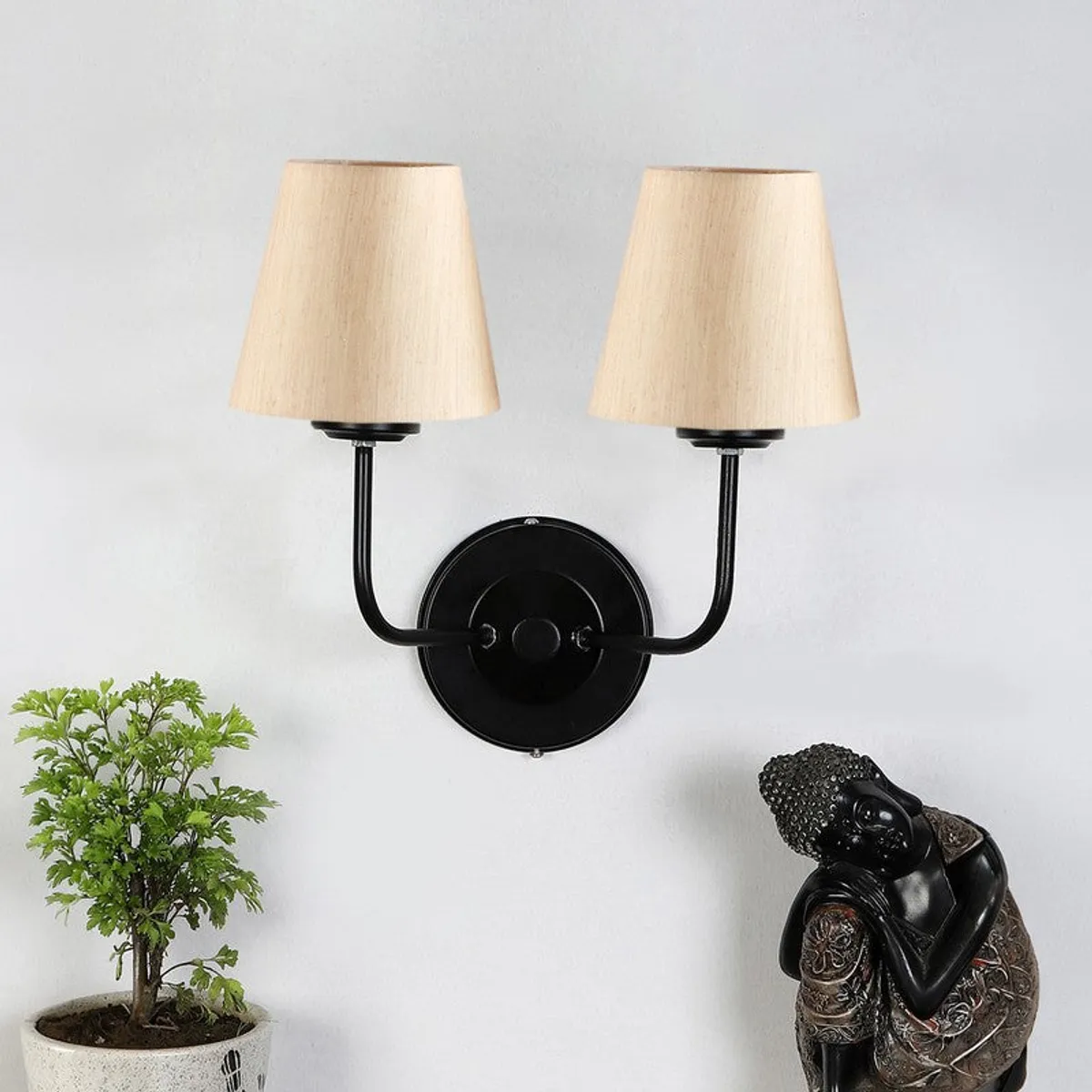Beige twin-shade wall lamp with black round backplate on a white wall