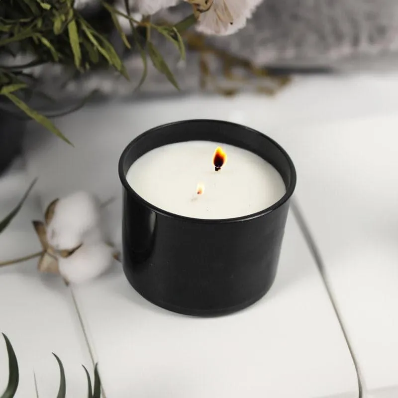 Black candle jar with white wax and a lit wick on a white surface