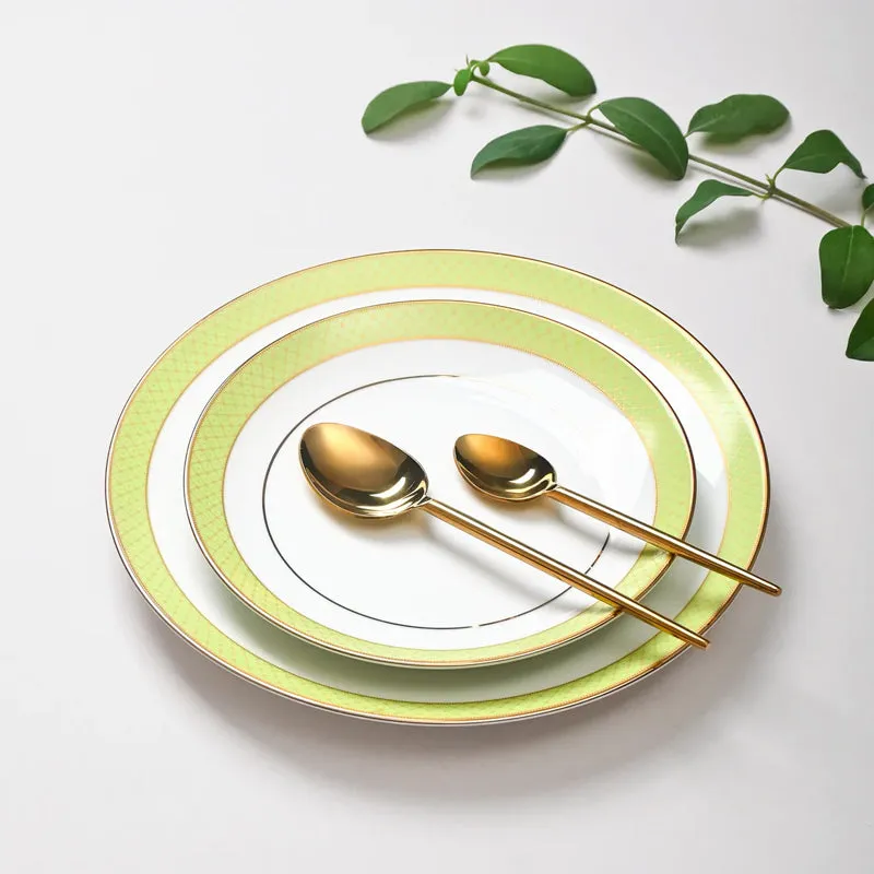 Stacked white plates with green and gold rims and two gold spoons