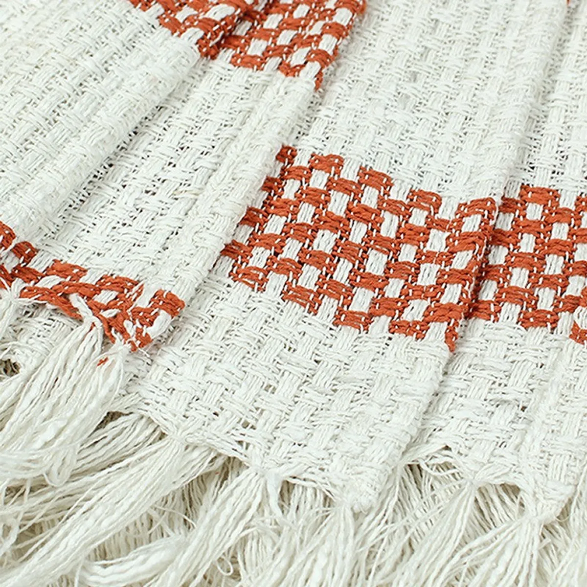 Close-up view of the throw's textured orange and cream pattern with fringe