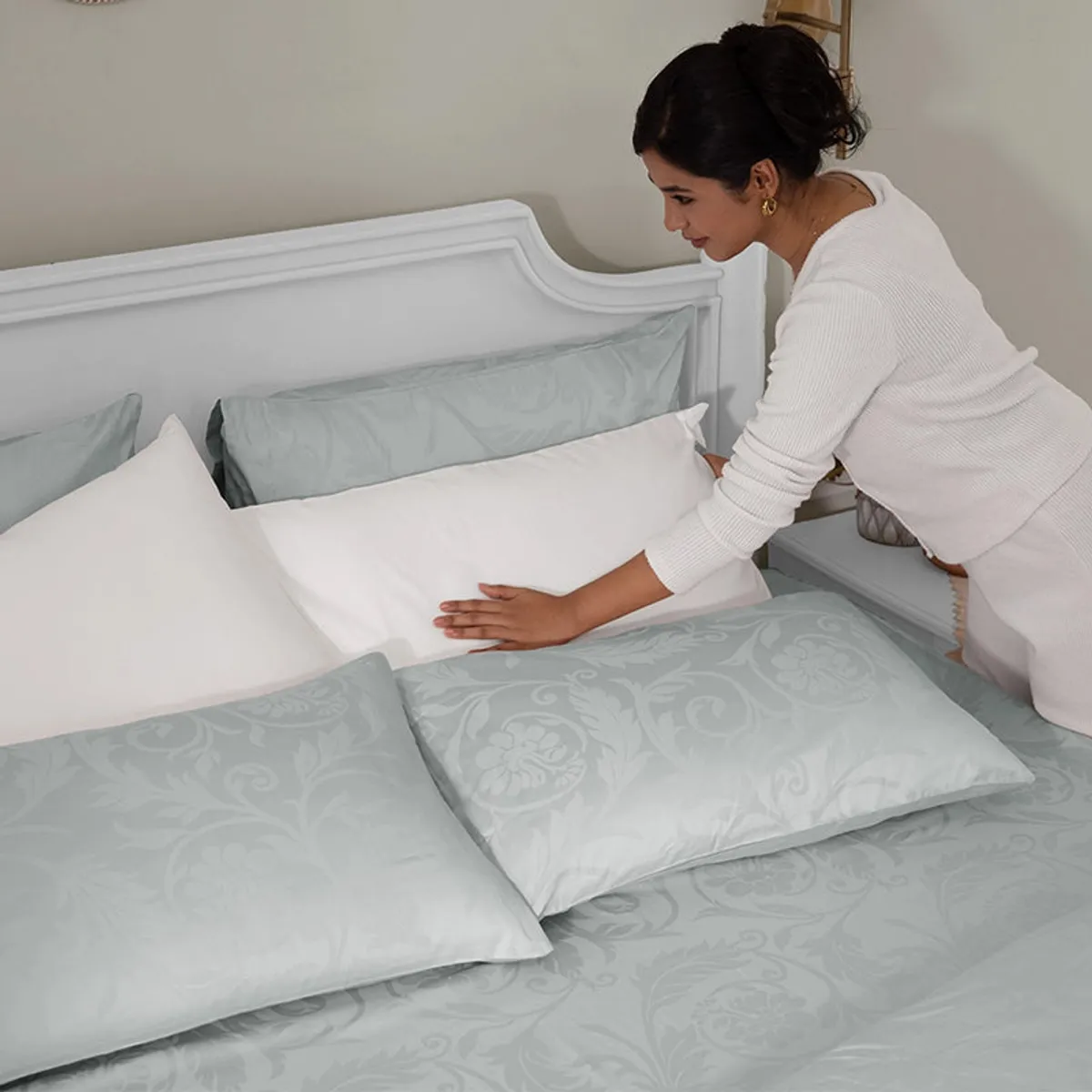 Person arranging pillows on a light grey floral duvet cover