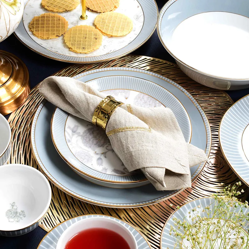 Grey and white floral dinnerware arranged with a napkin, gold accents and serving pieces