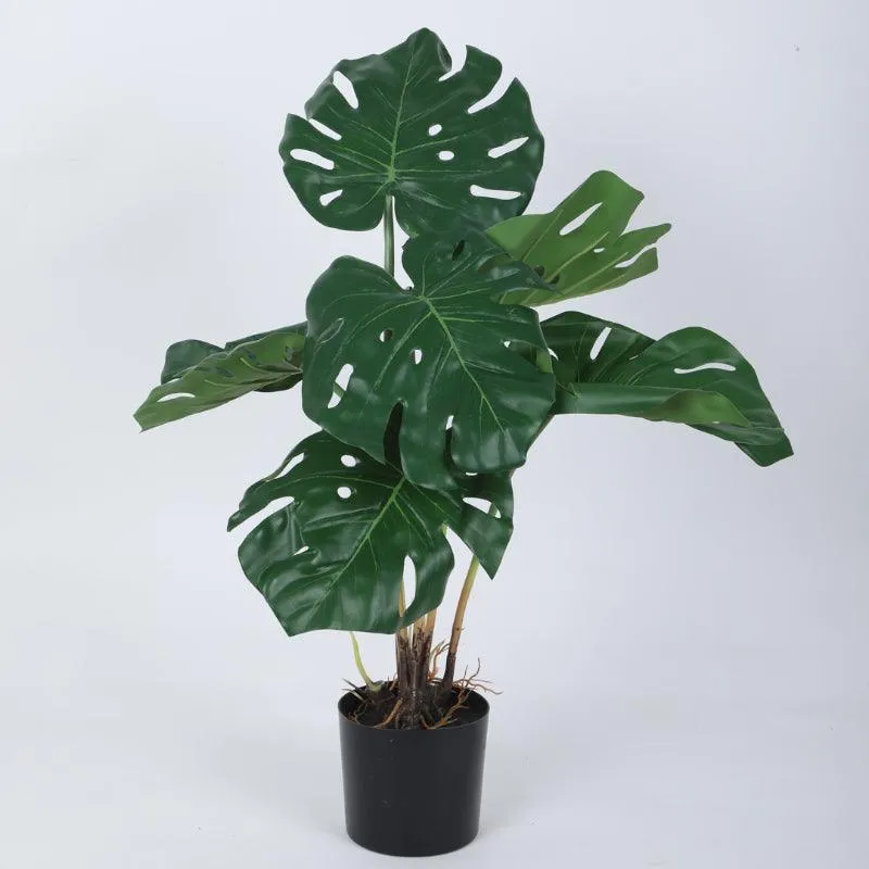 Single artificial Monstera plant with glossy split leaves in a black pot