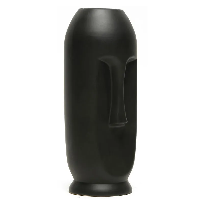 Side view of a tall matte black face vase on a white background.