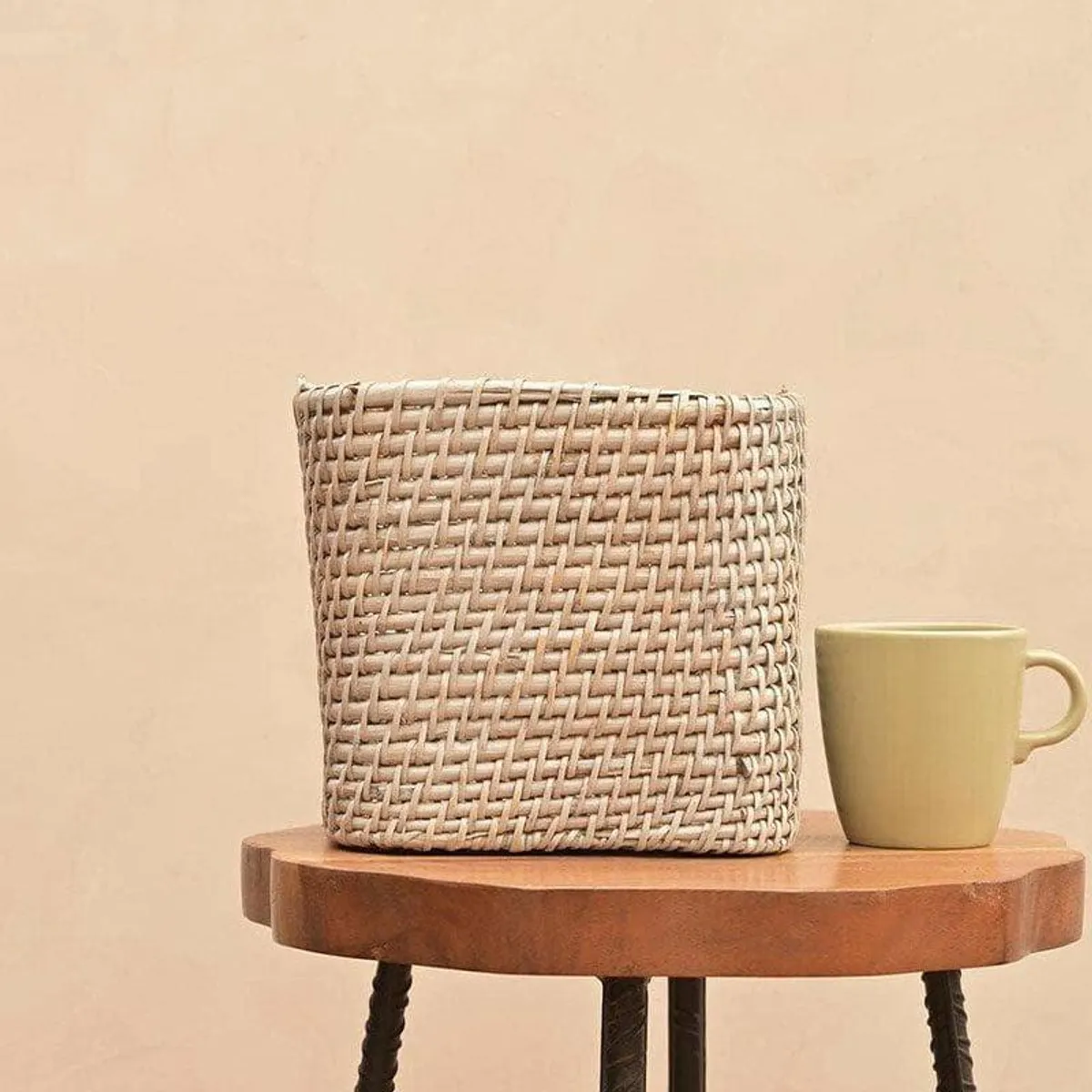 Beige square woven planter on a wooden stool beside a mug