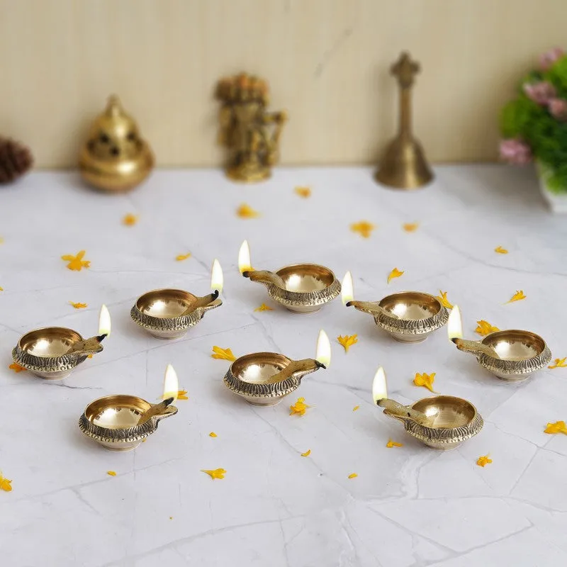 Set of lit gold brass diyas styled on a tabletop with decor accents