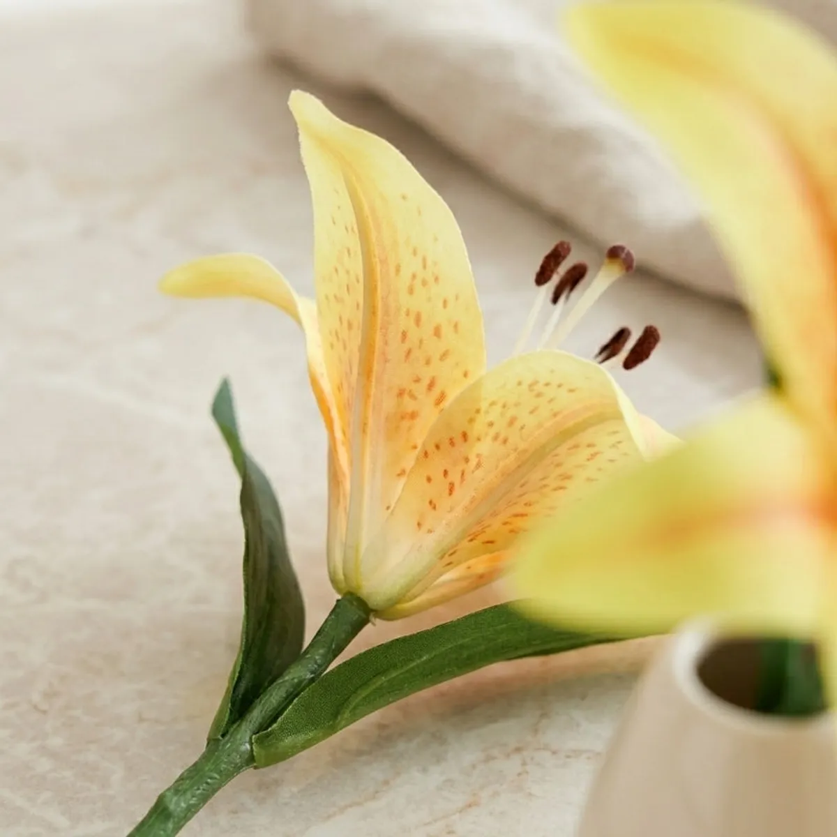 Close-up of a yellow artificial lily bloom with orange speckles and green leaves