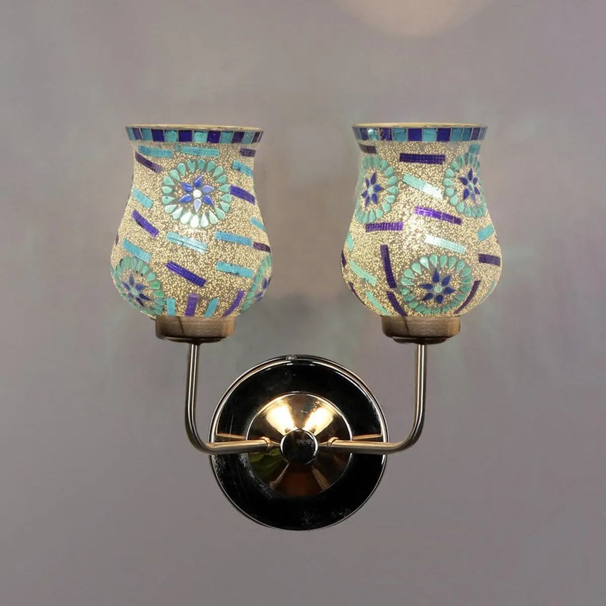 Dual mosaic glass wall lamp illuminated against a plain wall