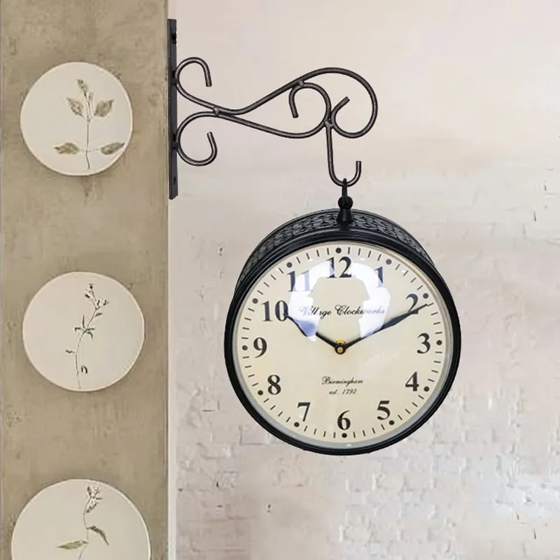 Black decorative wall clock with Roman numerals displayed against a white brick wall.