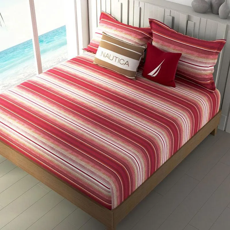 Striped orange bedsheet arranged on a bed beside a bright window