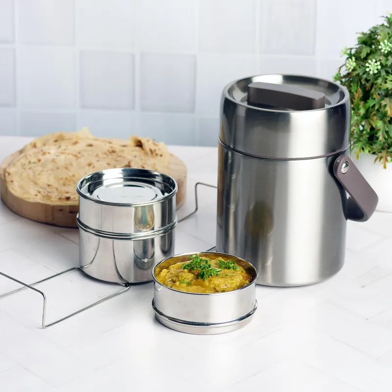Silver cylindrical stainless-steel tiffin carrier with stacked containers and food on a kitchen counter