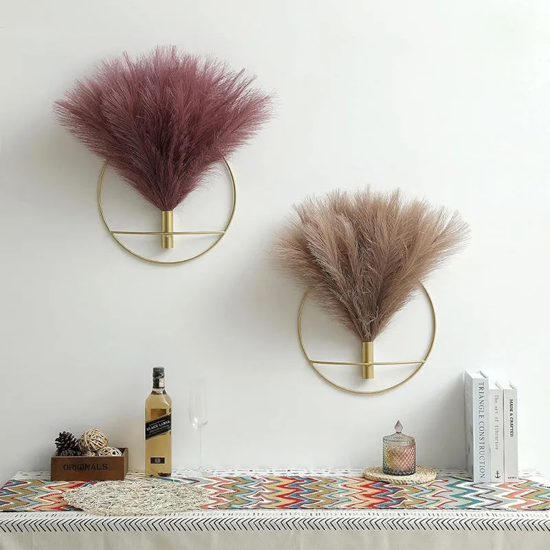 Two gold circular wall vases with fluffy burgundy and beige stems above a console