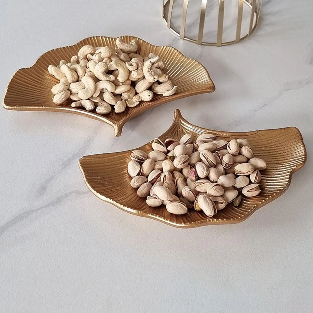 Two gold ginkgo leaf-shaped platters filled with nuts on a light surface