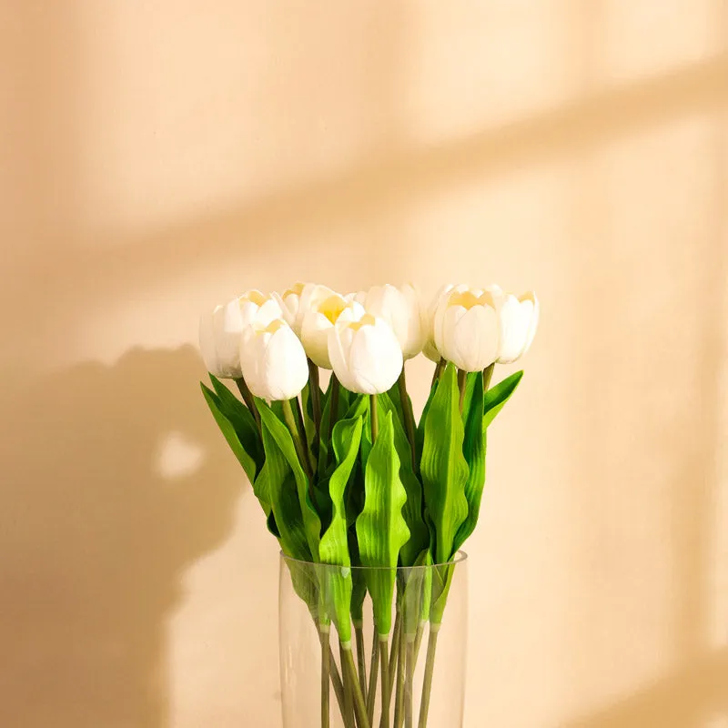 Close-up of white tulip blooms with green leaves in a vase