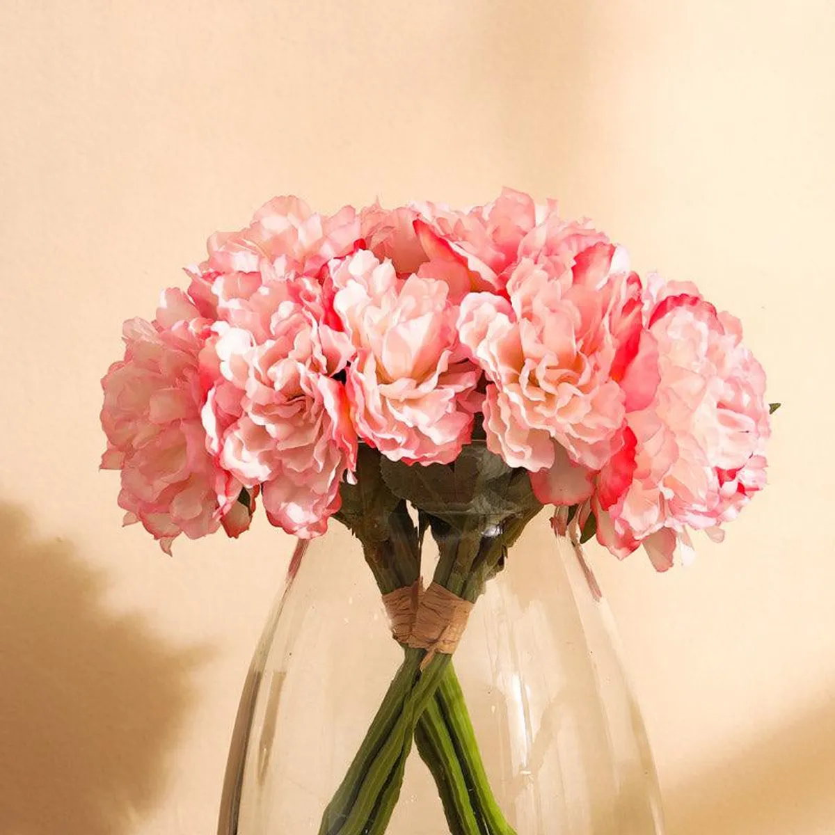 Close view of baby pink artificial peony bouquet in a clear glass vase