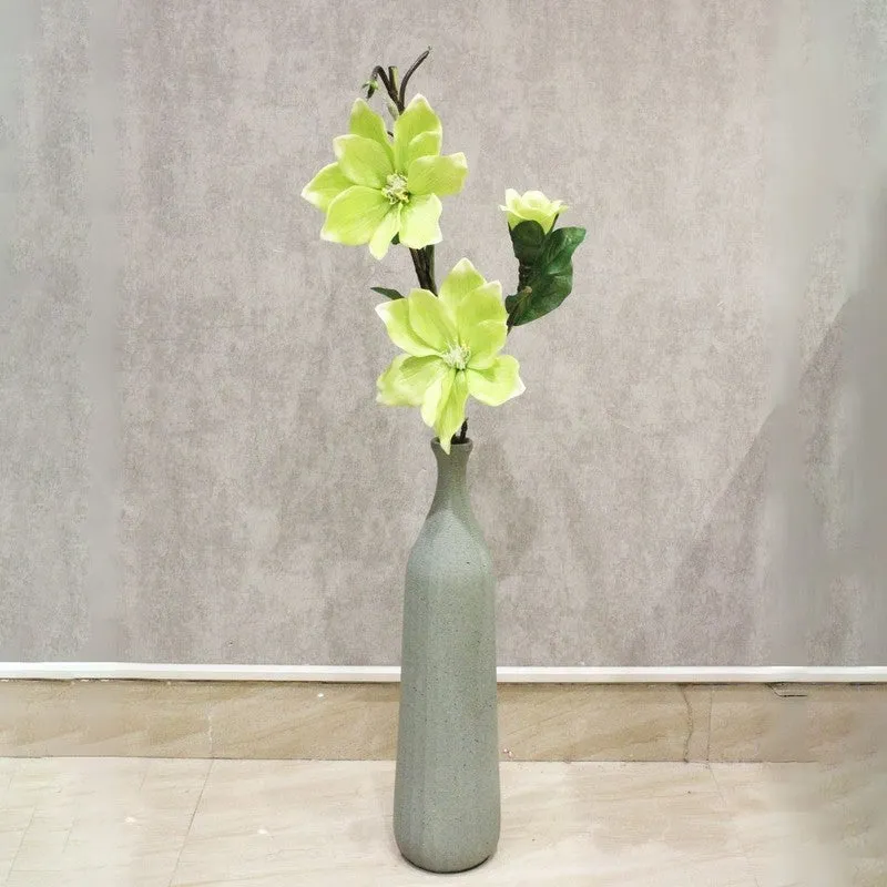 Green artificial magnolia flower stick displayed against a neutral wall