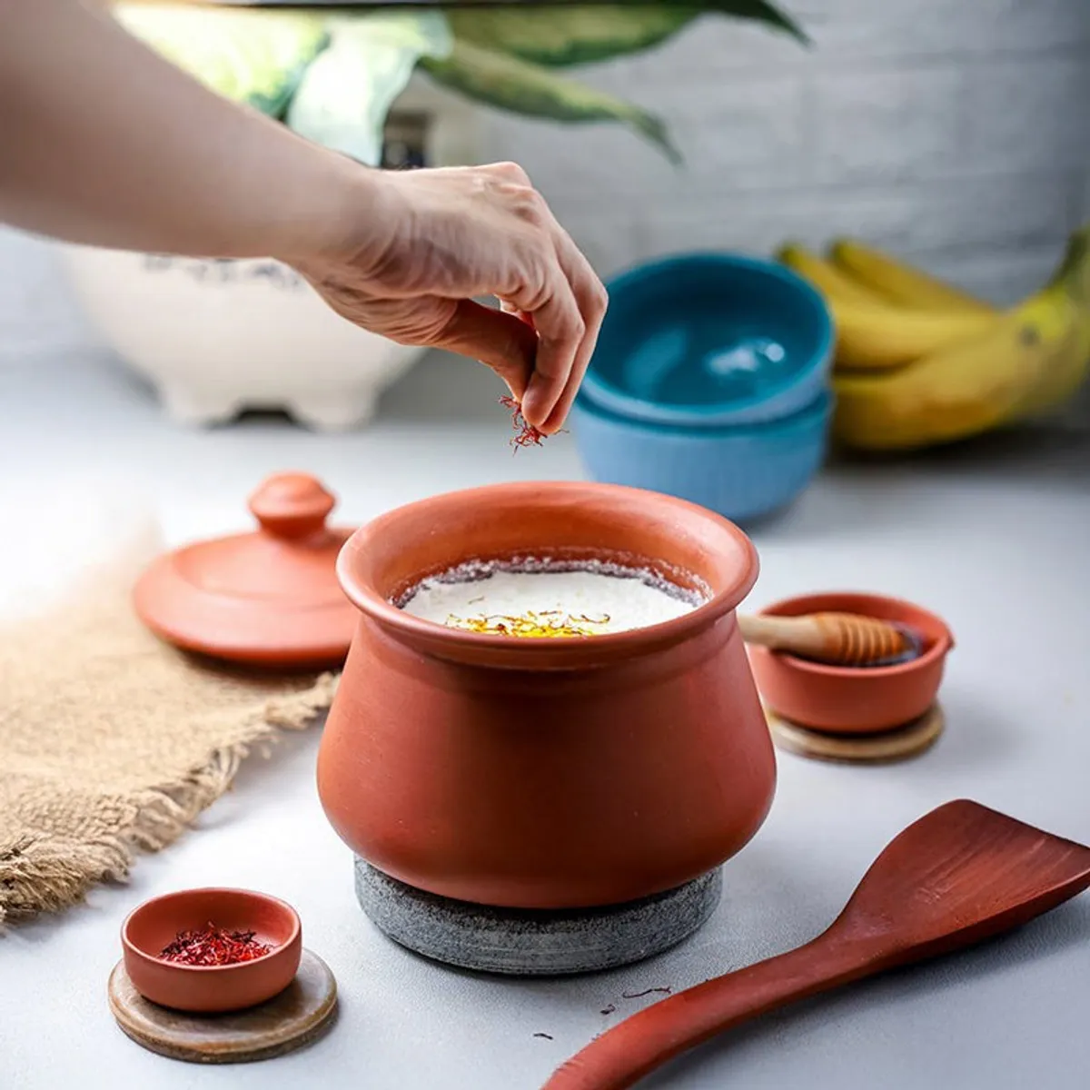 Brown terracotta handi with lid and serving accessories on a kitchen counter
