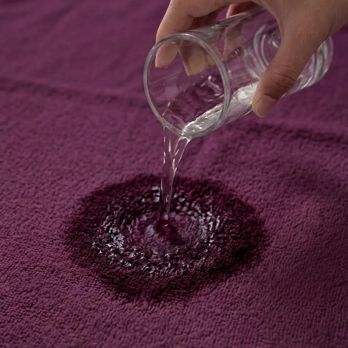 Water being poured onto the absorbent surface of a wine-purple towel