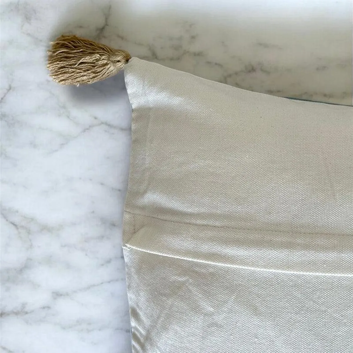 Close-up of the plain reverse fabric and gold tassel corner of a cushion cover