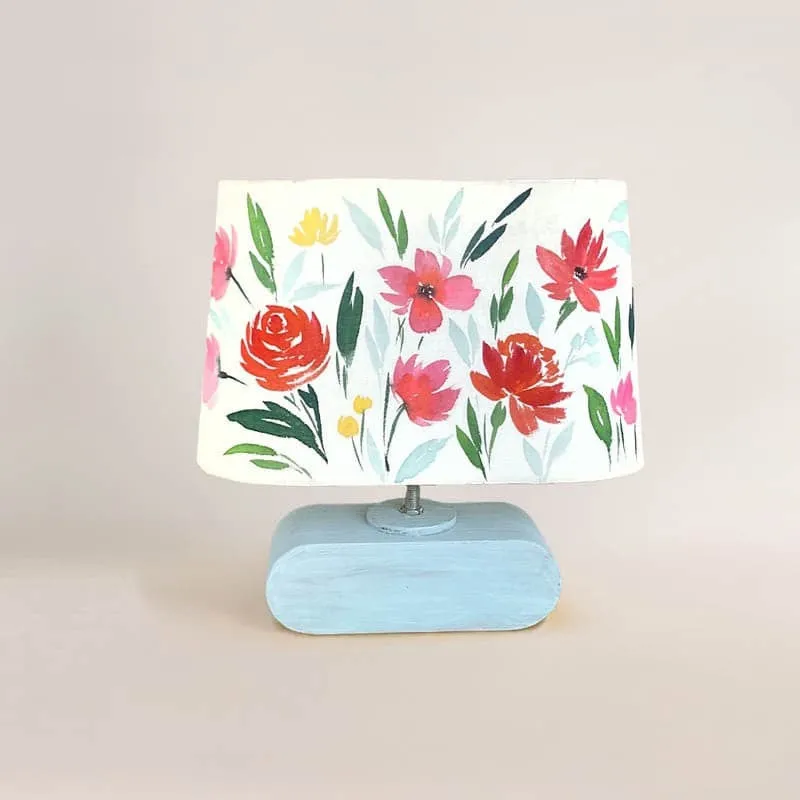 Handpainted floral fabric table lamp with a light blue base on a plain background