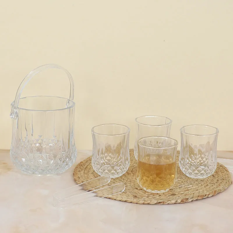 Transparent glass ice bucket, four glasses and tongs on a woven mat