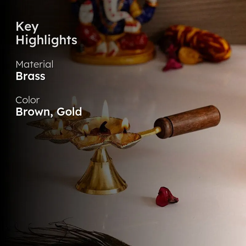 Lit gold-toned panchdeep diya with a brown wooden handle in a festive setting