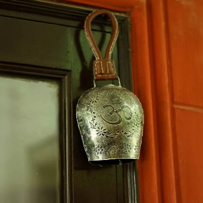 Silver bell with floral detailing displayed against a dark door and orange wall