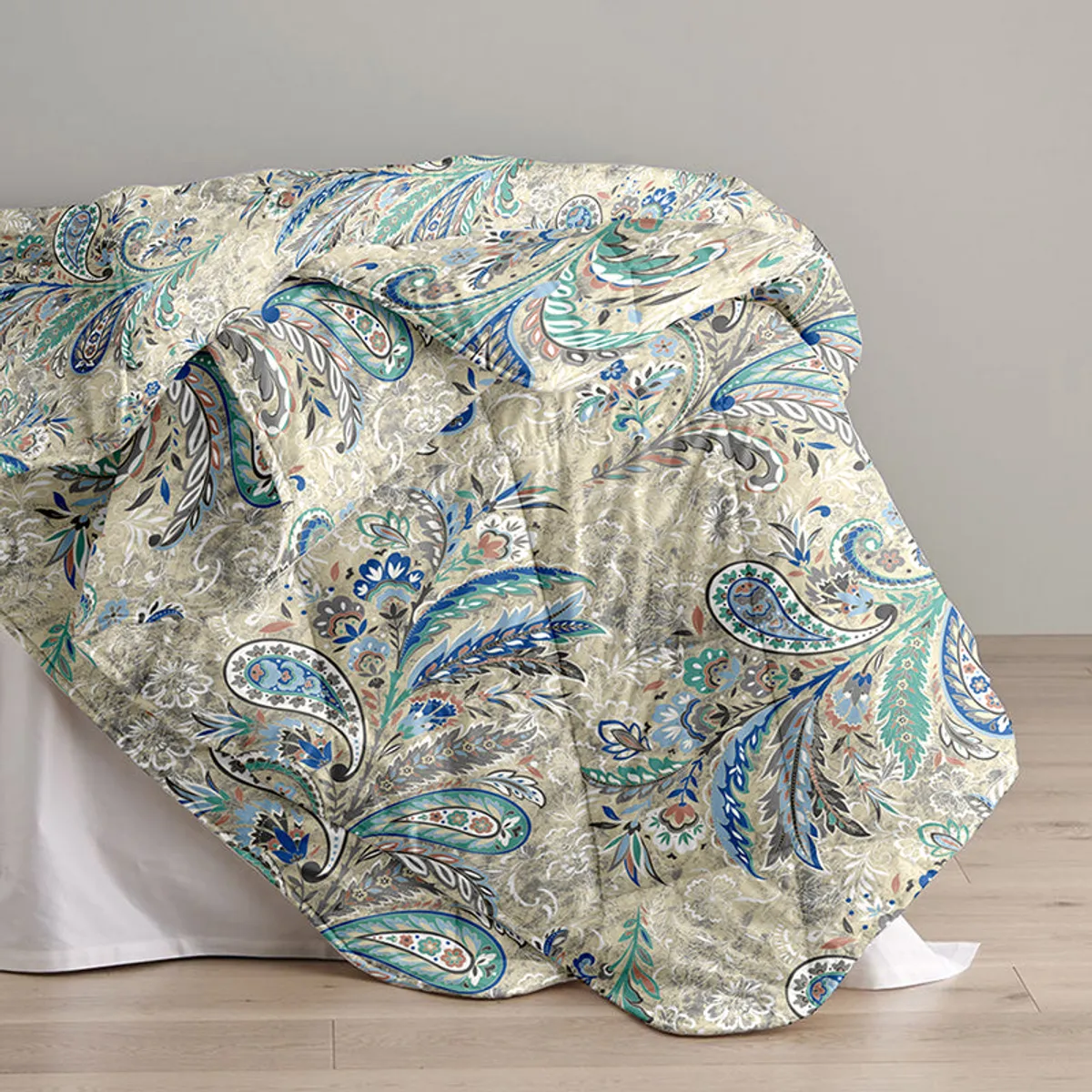 Paisley comforter draped over a bed against a neutral wall