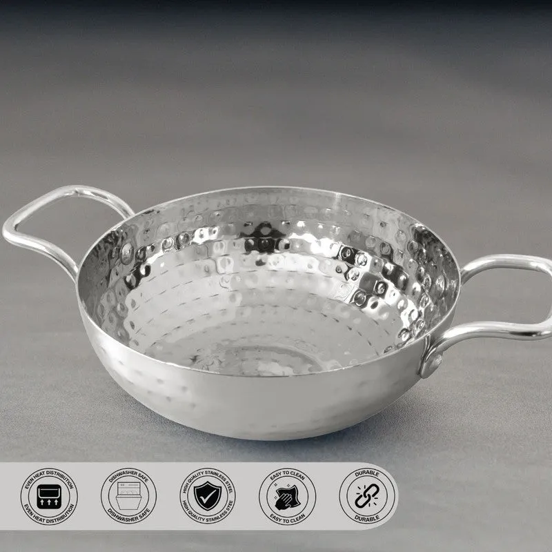Empty silver hammered kadhai with two side handles on a dark background