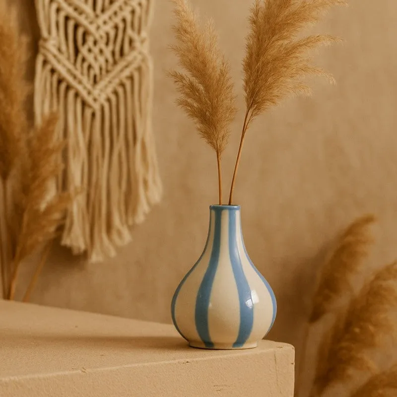 White and blue striped vase with tall dried stems against a warm neutral backdrop