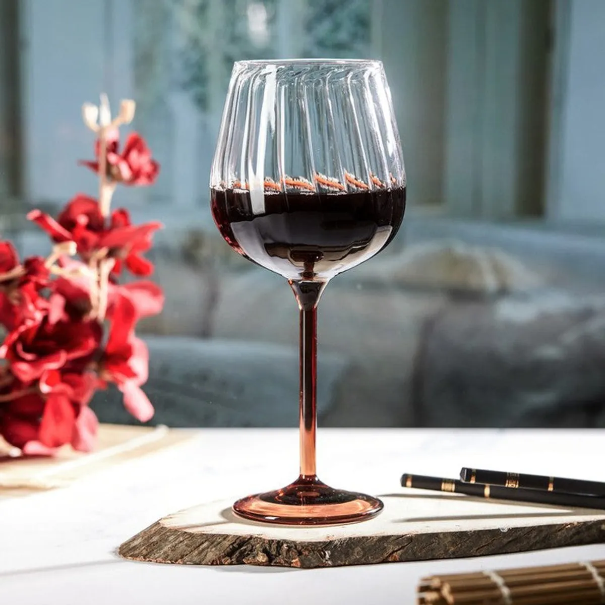 Single ribbed wine glass with tawny stem filled with red wine on a bright table