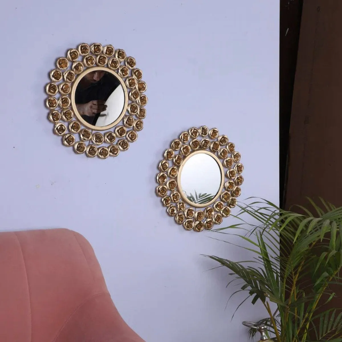 Two gold rose-framed round mirrors displayed on a light wall beside a chair and plant
