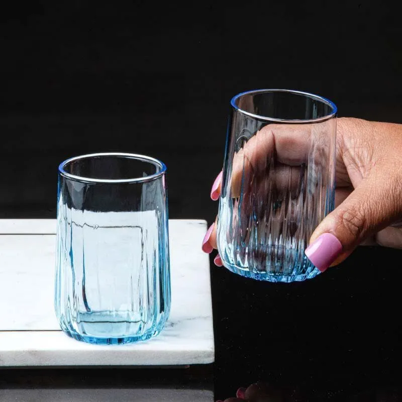 Two blue ribbed glass tumblers, one held in hand against a black background